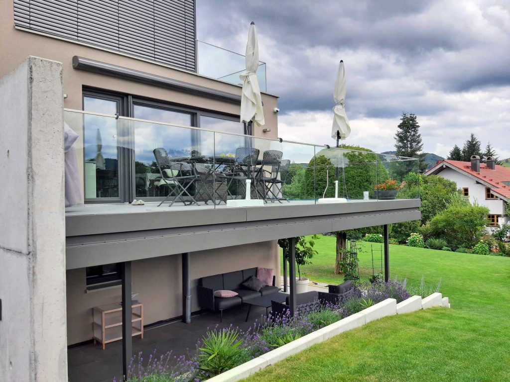 Stahlbalkon mit Ganzglasgeländer am Haus angebracht. Mit Aluminiumblenden zur Verkleidung des Fußbodenaufbaus. Alle Metallteile sind Farbig pulverbeschichtet.