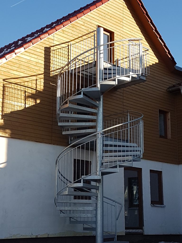 2-geschößige Spindeltreppe aus einer Verzinkten Säule mit angeschraubten Stufenträgern mit Gitterrostfüllung. Umlaufendes Geländer aus Rundrohr mit vertikalen Füllstäben aus Rundstab