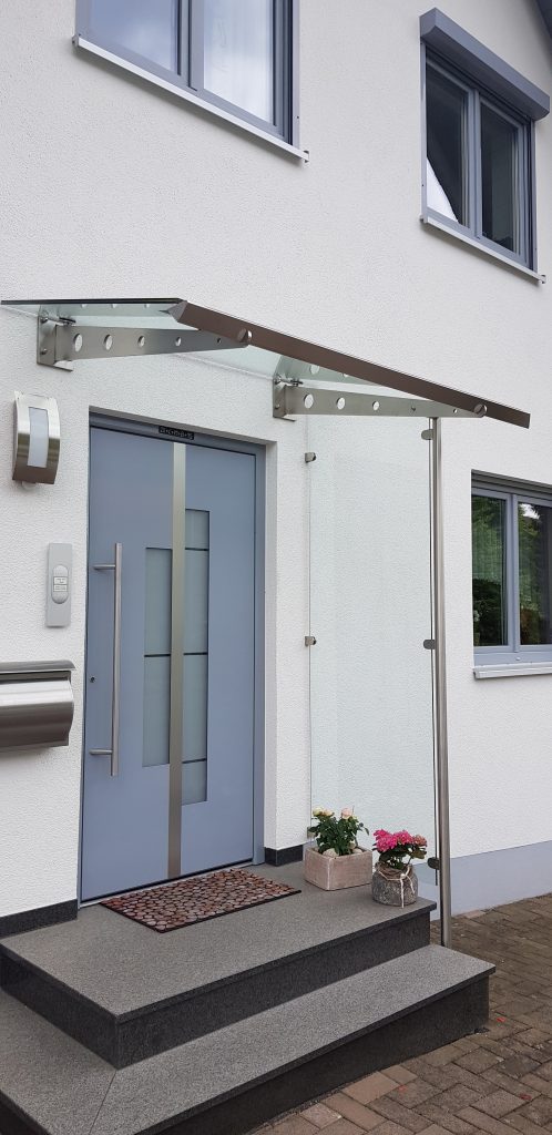 Vordach aus an Wand befestigter Edelstahlkragarme mit Glasscheibe belegt und Edelstahlrinne, sowie mit feststehendem Seitenteil mit Glasfüllung