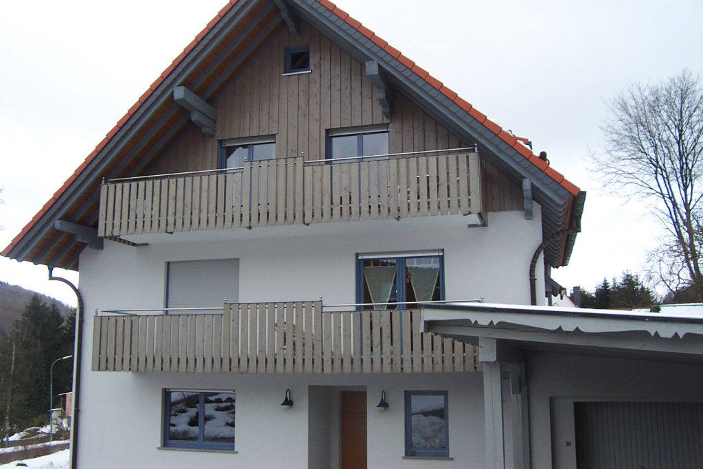Balkongeländer an einem Einfamilienhaus, mit vertikaler Füllung aus Holzbrettern. Stahlteile aus Edelstahl Rostfrei, gebürstet.
