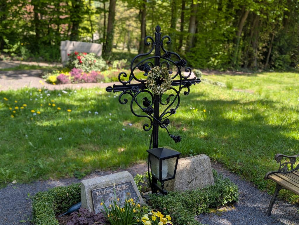 Schmiedeeiserenes Grabkreuz mit geschmiedeten Rosenranken auf Sandsteinsockel. Feuerverzinkt und schwarz pulverbeschichtet.