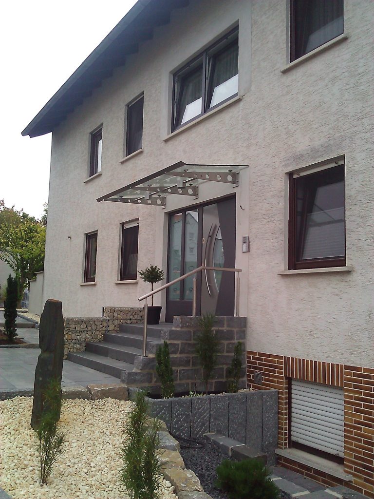 Vordach aus an Wand befestigter Edelstahlkragarme mit Glasscheibe belegt und Edelstahlrinne